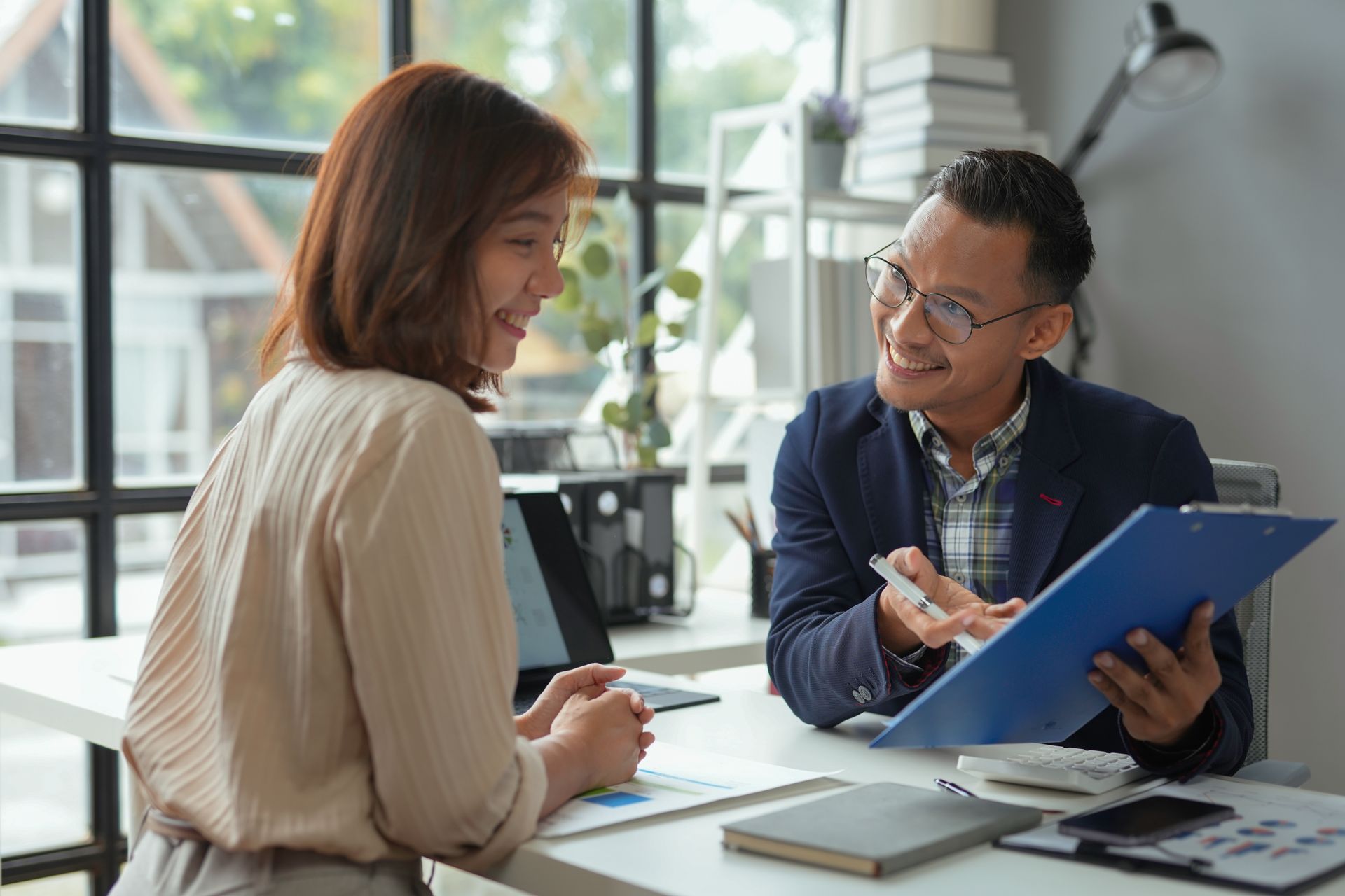 Woman and man reviewing documents at a desk, both smiling, indoor office setting.