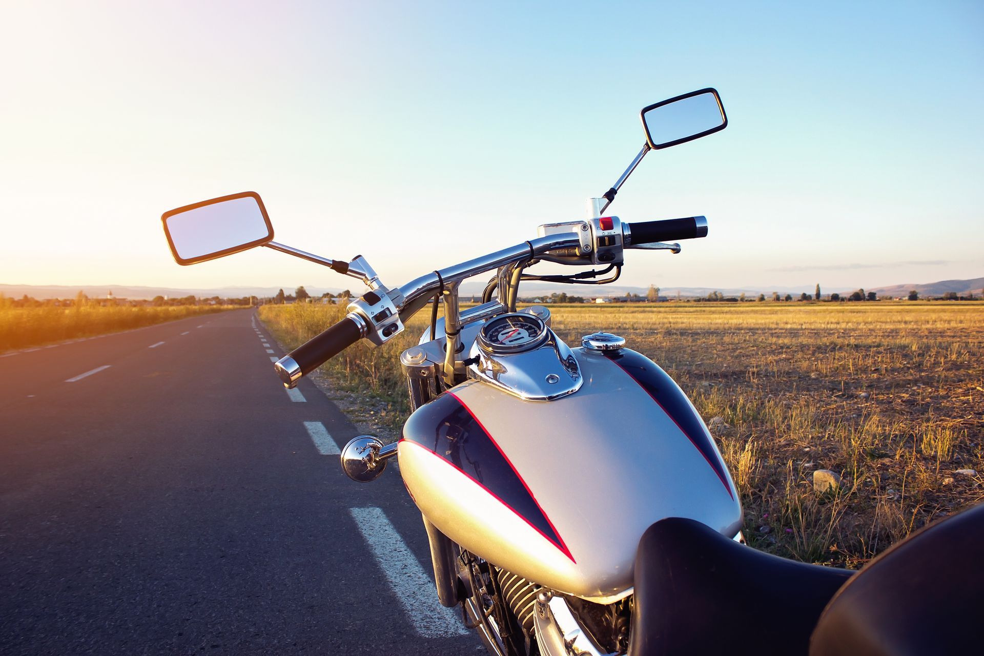 Motorcycle parked on a road at sunset, with a view of fields and a clear sky.