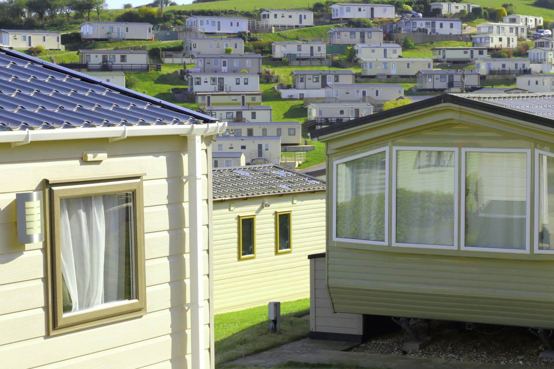 Mobile homes on a hillside, with white exteriors. Sunny day, green grass, blue skies.