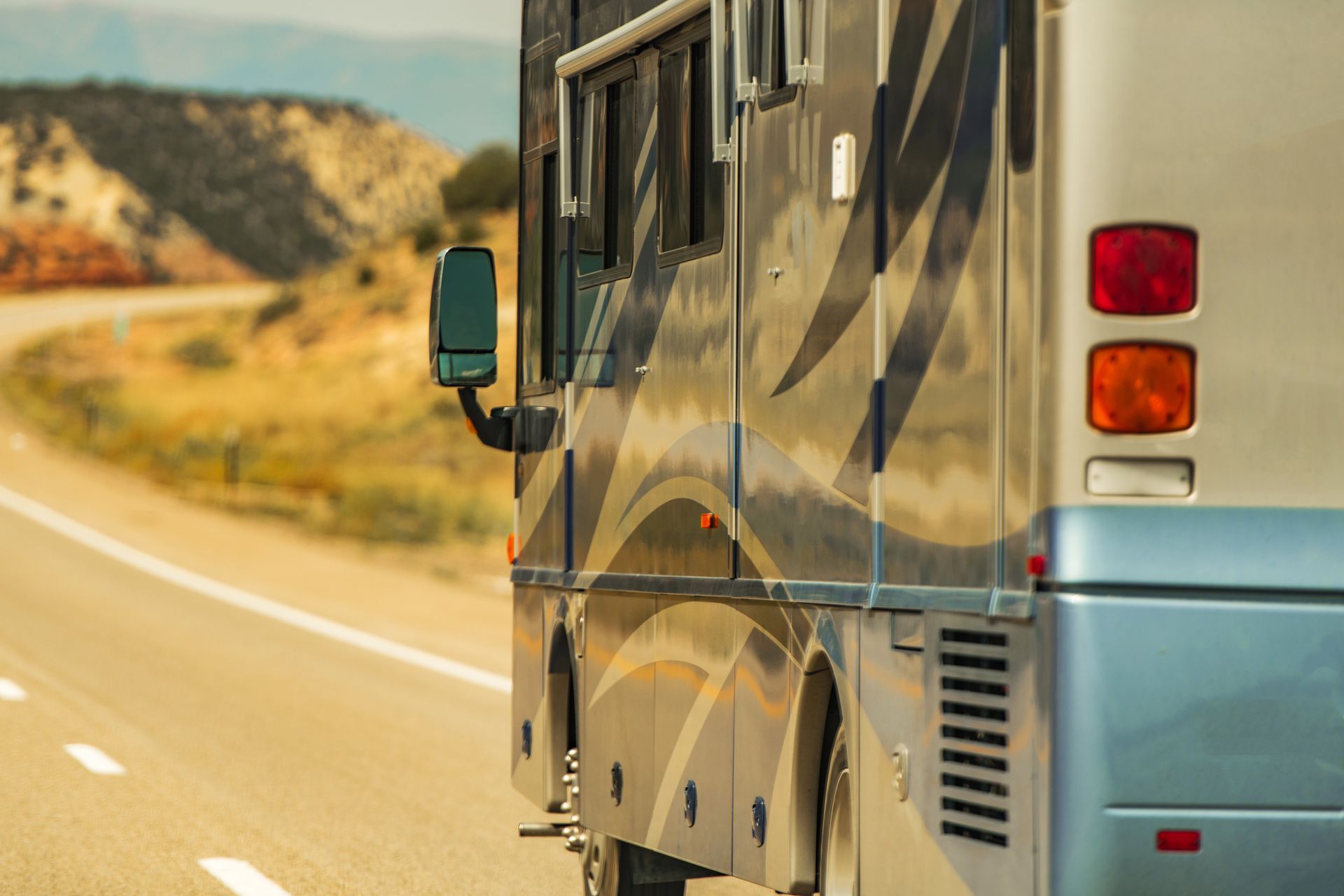 RV driving on a desert road with mountains in the background.