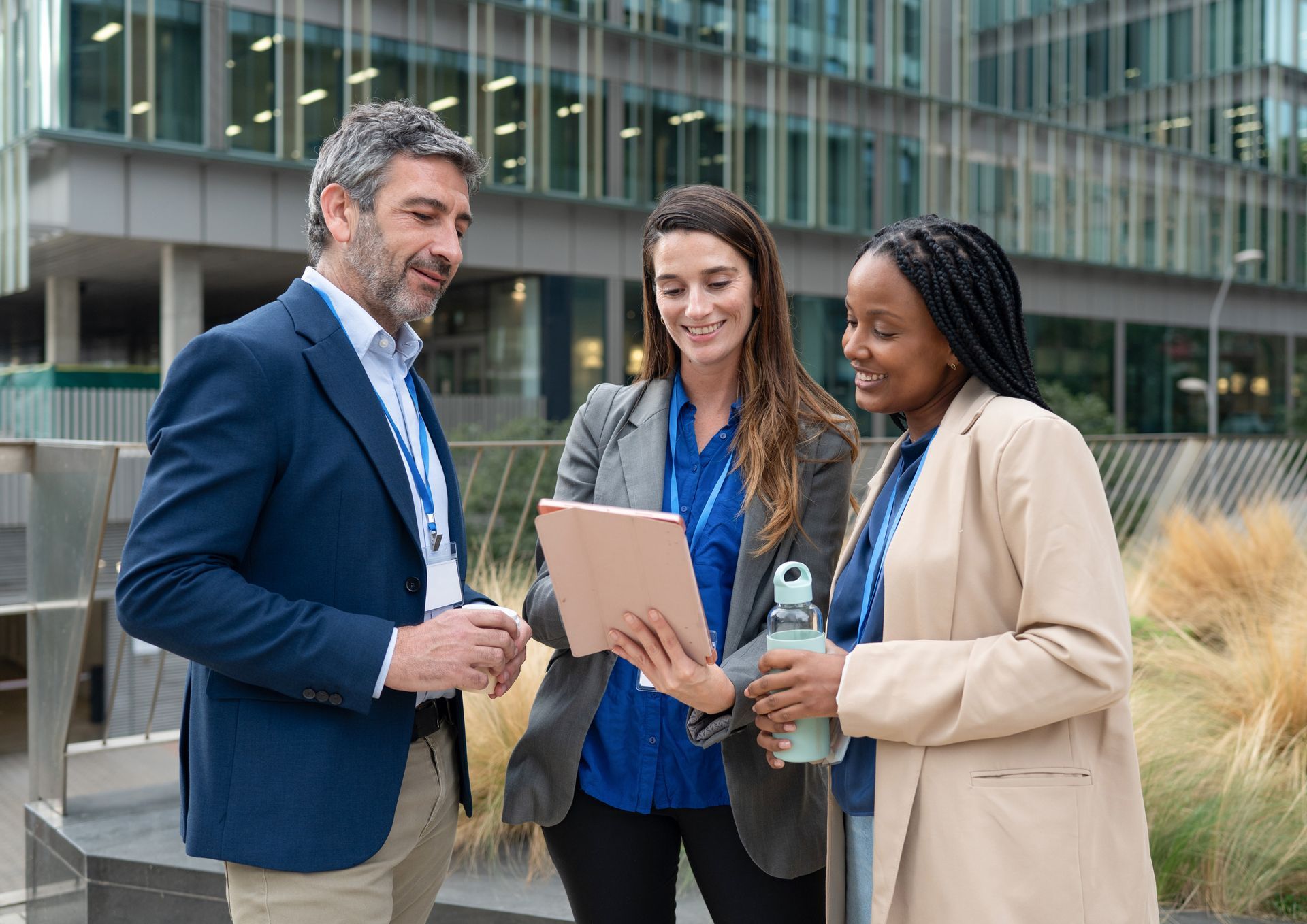 Three people, outdoors, looking at a tablet. Modern building background.
