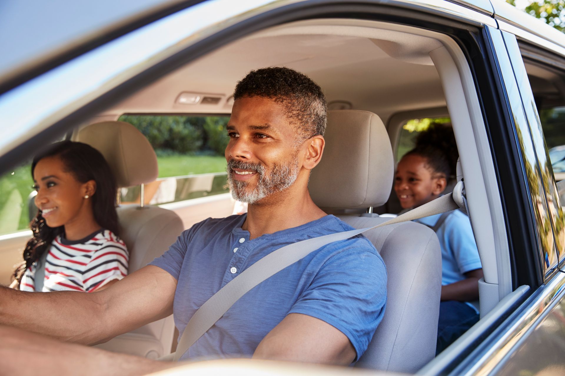 Man driving car with two children. Sunlight, smiles, seatbelts.