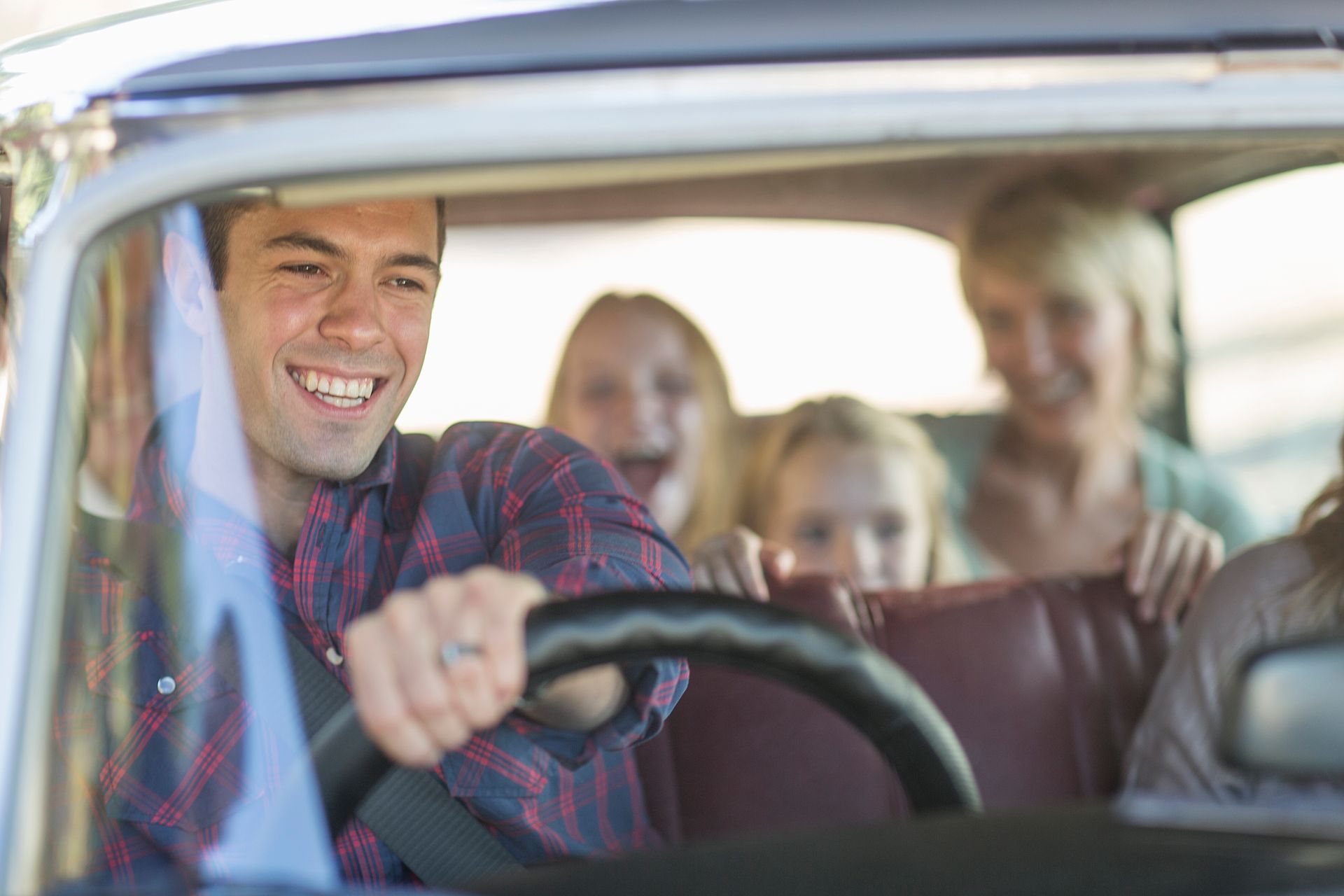 Man driving car, smiling, with family in the back seat.