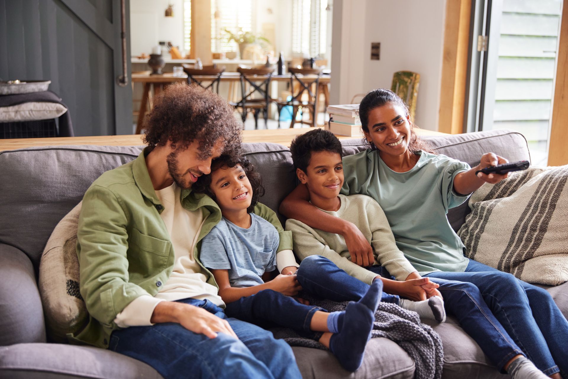 Family of four sitting on a couch, watching TV together.