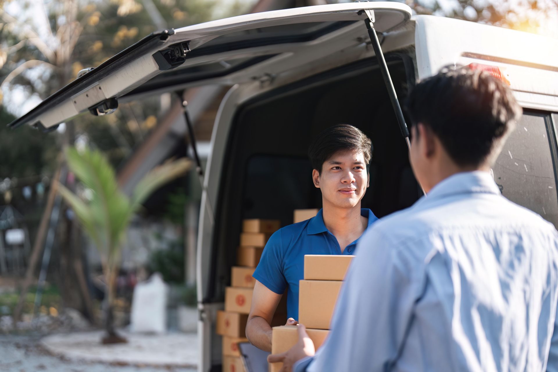Delivery person handing packages to a recipient from a van, outdoor setting.