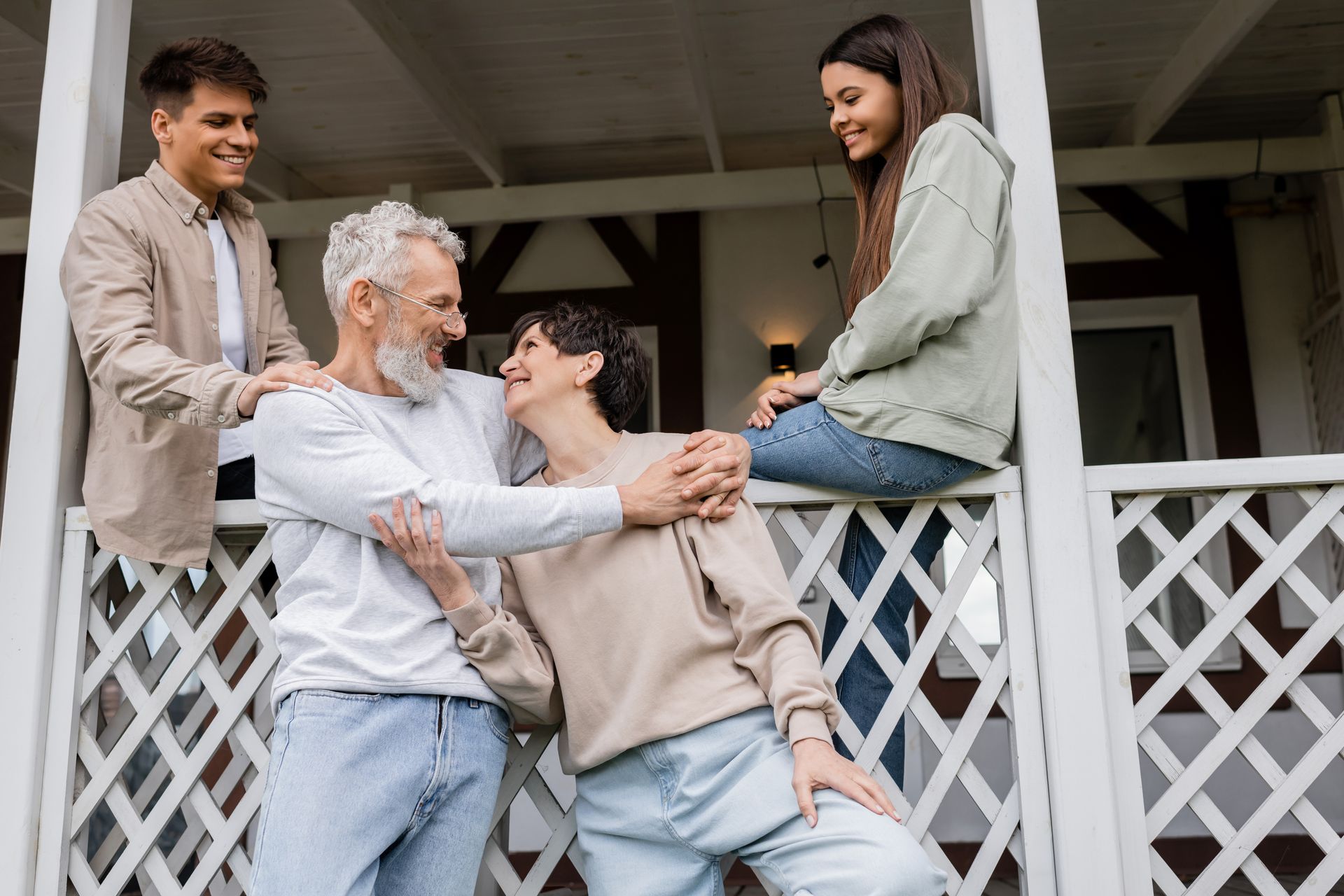 Family embracing on a porch: grandparents with their children, smiling, happy.