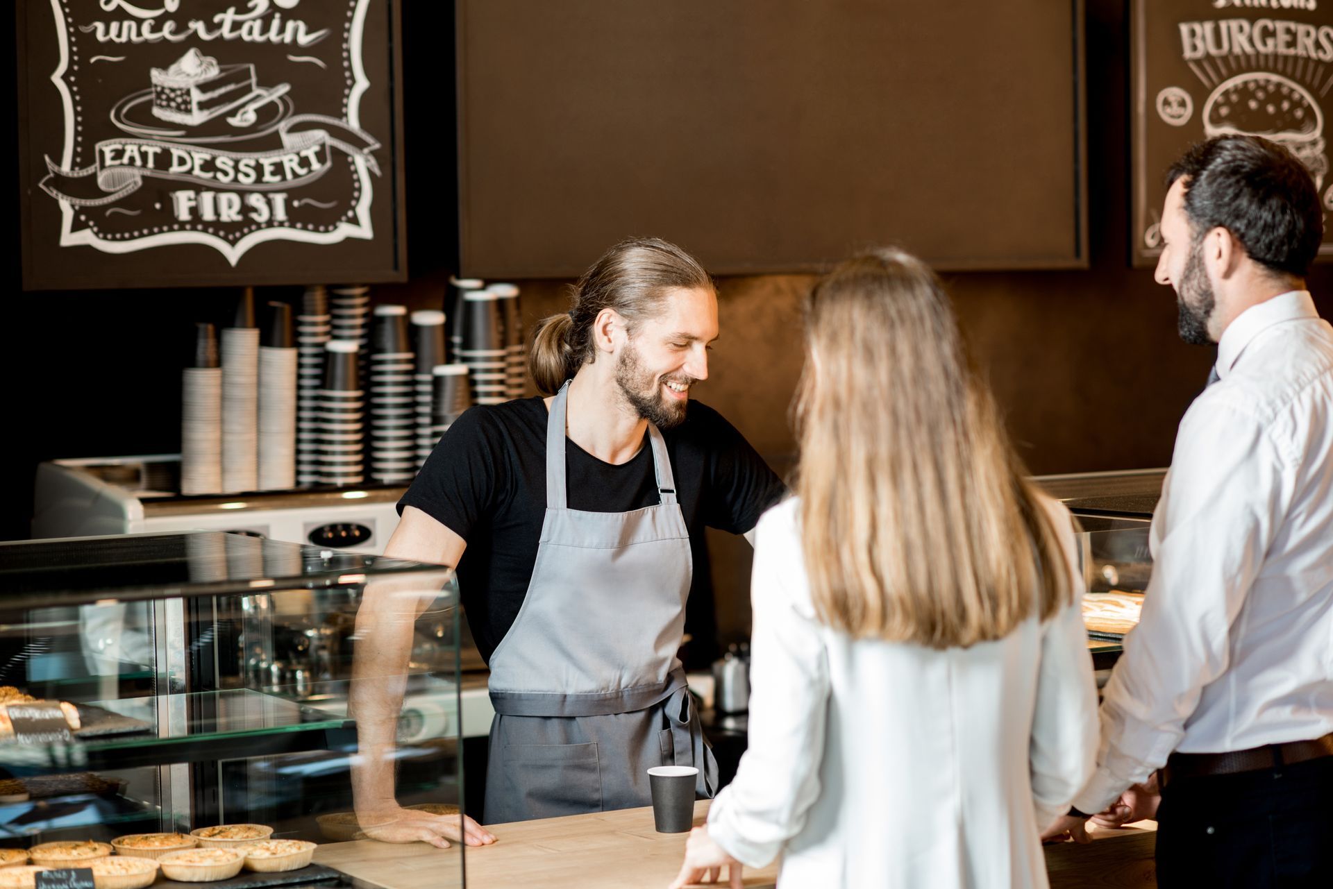 Barista smiling, taking an order from a couple at a cafe counter.