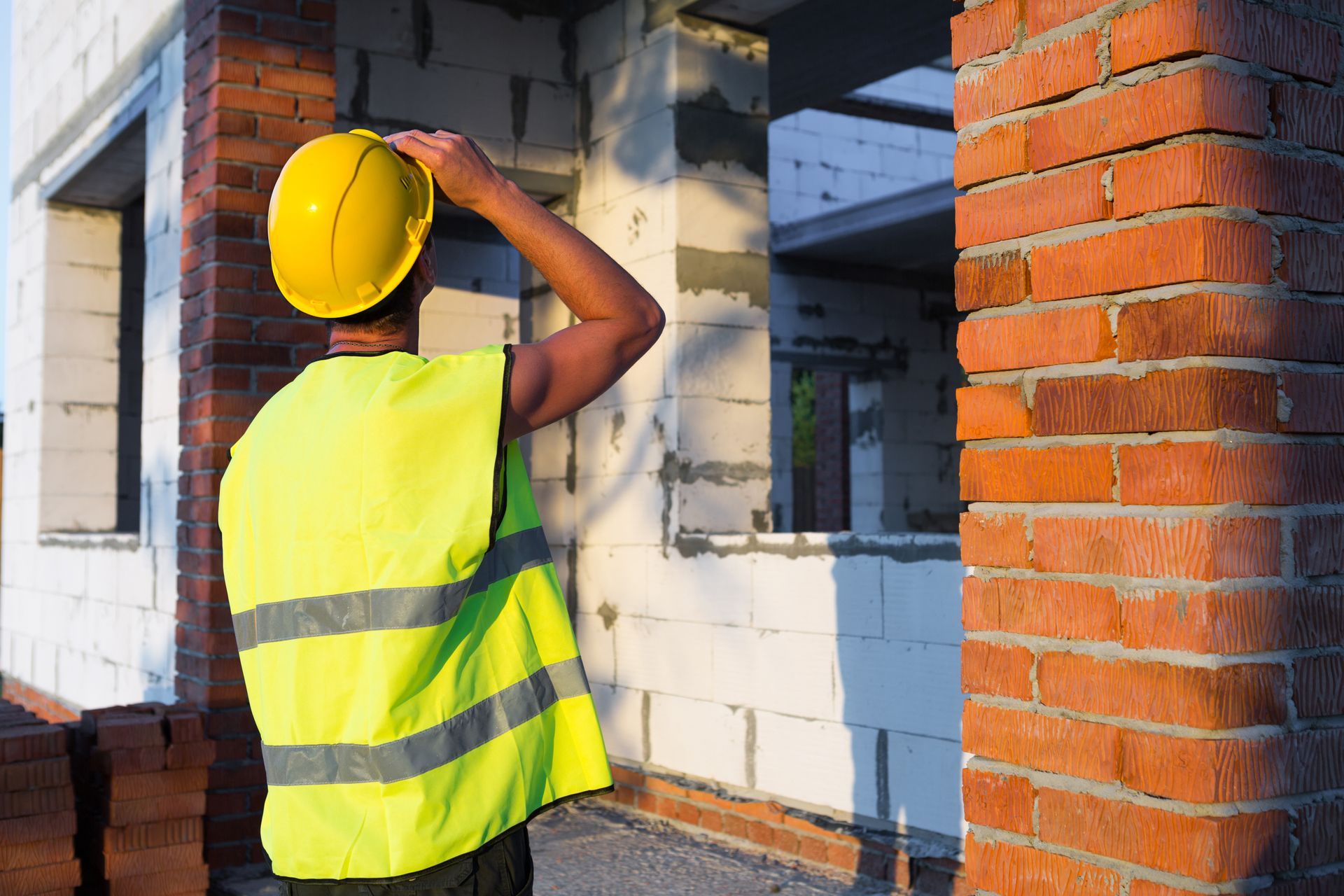 Construction worker in yellow vest and hard hat surveying a building under construction.