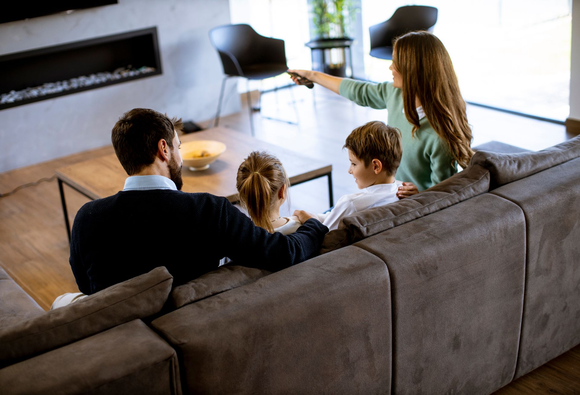 Family on couch watching TV; woman holding remote. Modern living room.