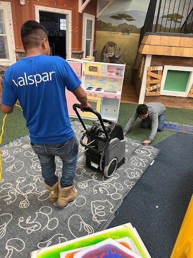 A man in a blue shirt is standing next to a vacuum cleaner in a room.