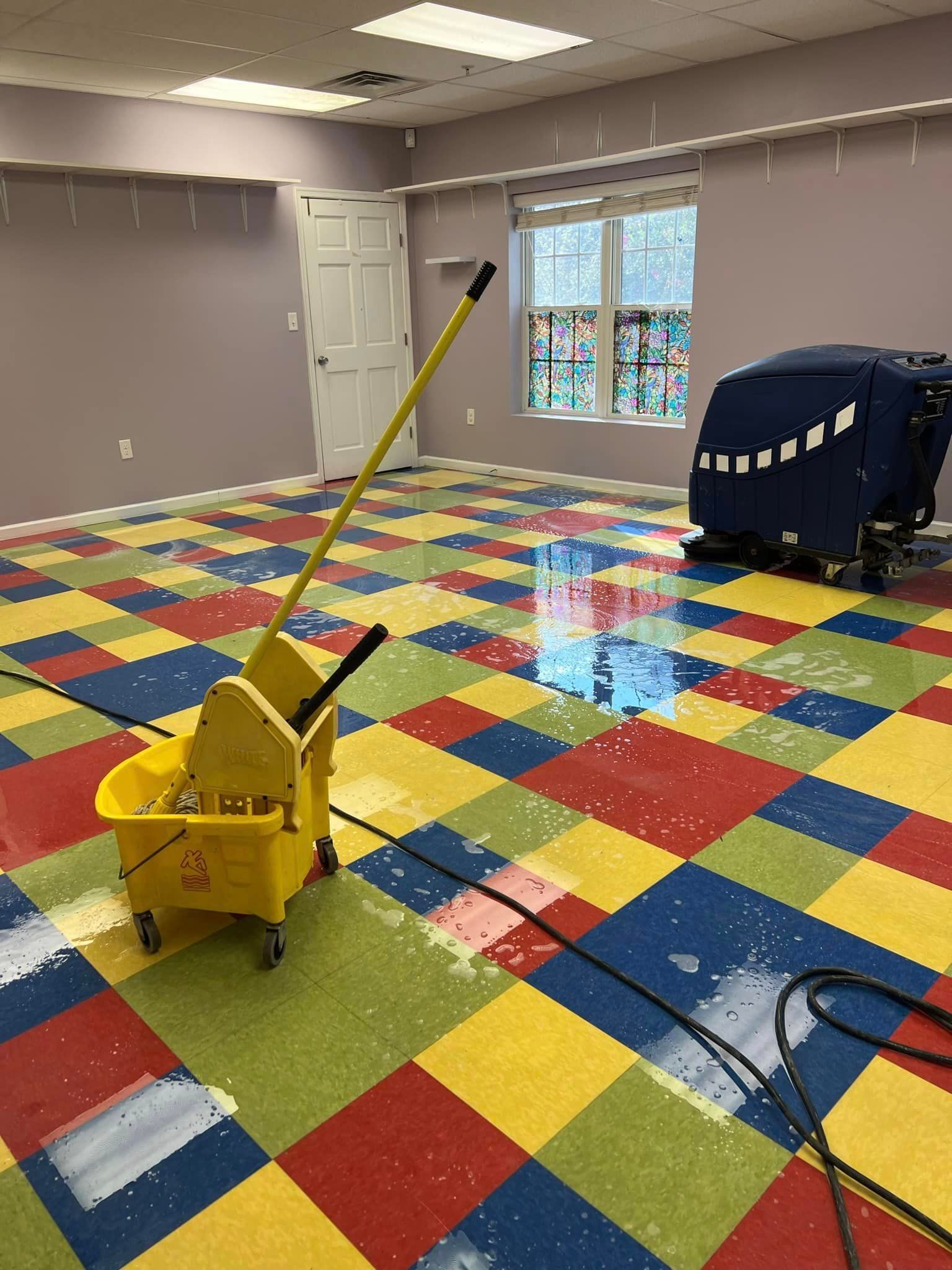 A yellow mop and bucket are sitting on a colorful checkered floor.