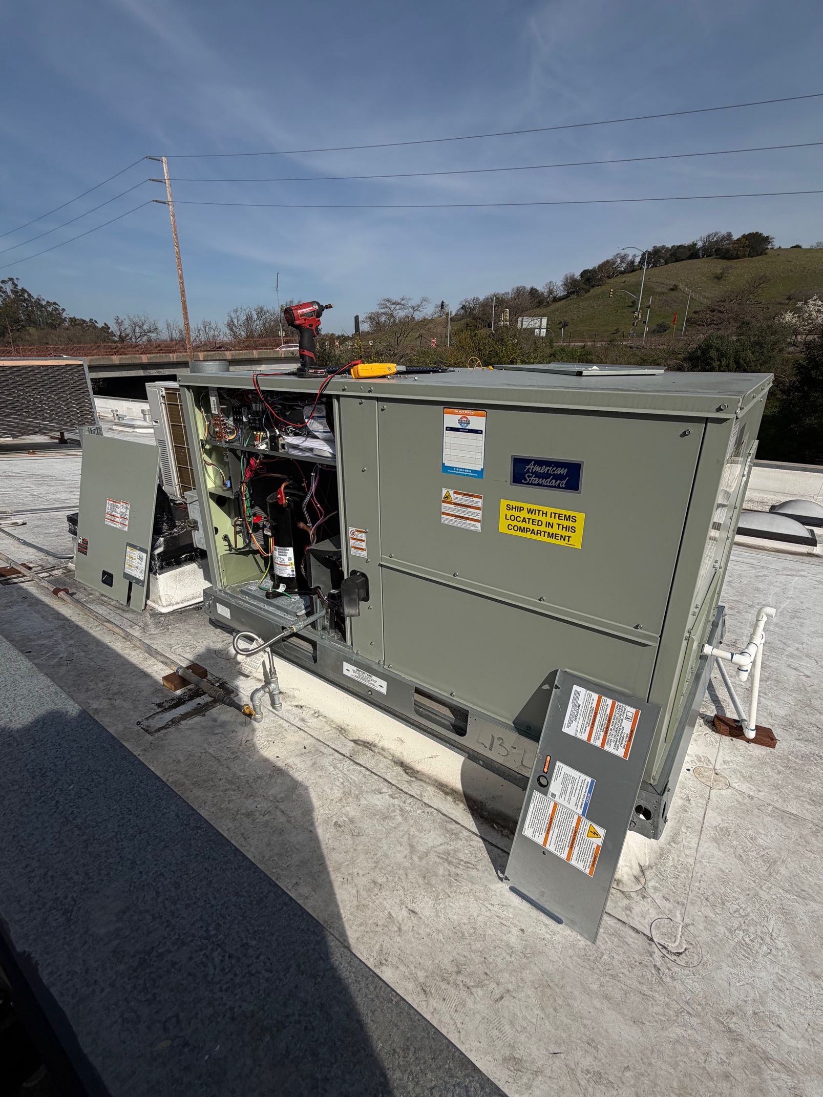 Rooftop HVAC unit with open panels. Gray exterior, yellow labels, electrical components visible inside.