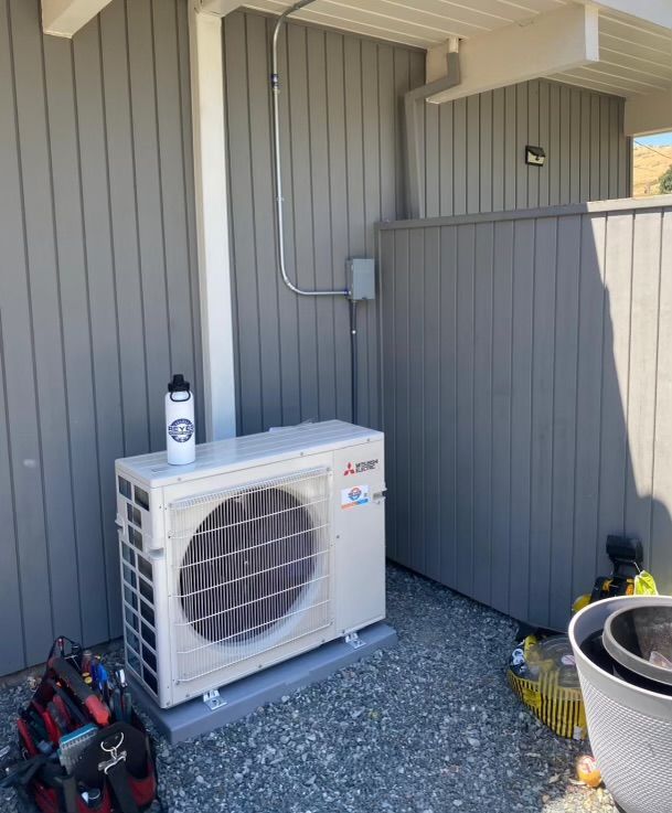 A white air conditioner is sitting on the side of a building — Novato, CA — Reyes Heating and Air Inc.