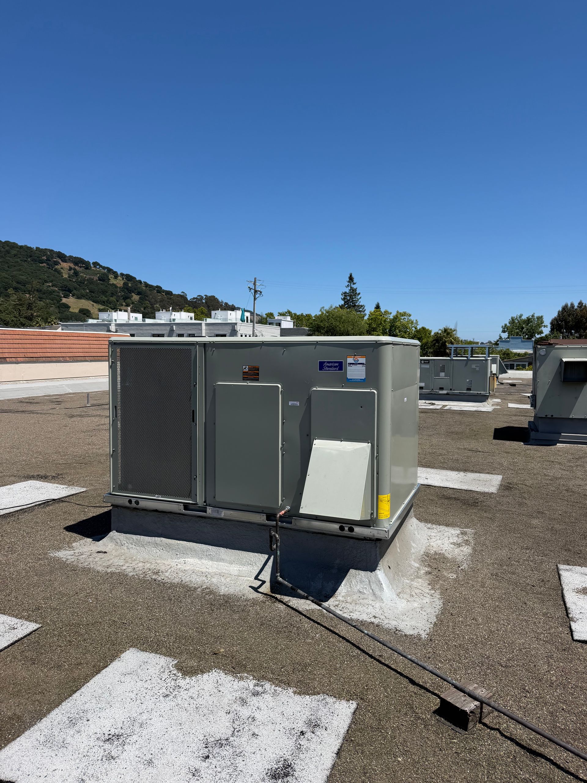 Gray rooftop HVAC unit on gravel with white markers under a clear blue sky