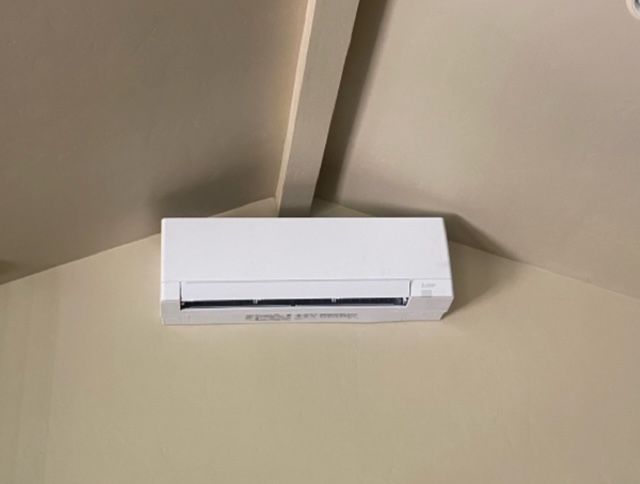 A white air conditioner is sitting in the corner of a room.