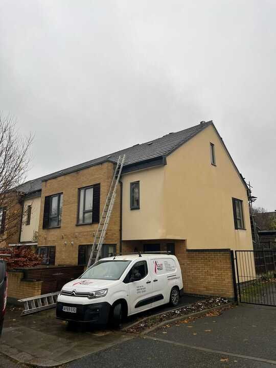 A white van is parked in front of a building with a ladder attached to it.