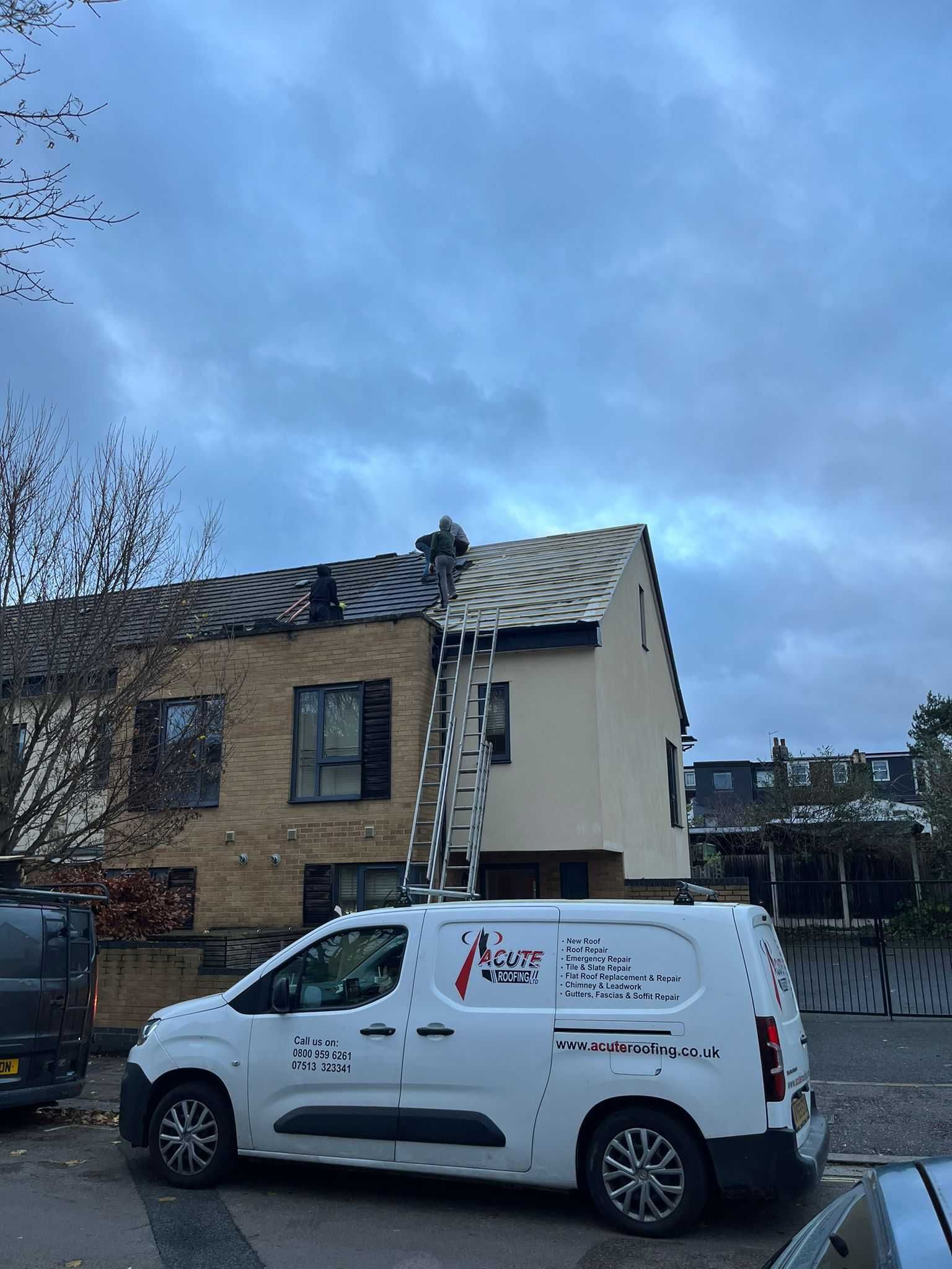 A white van is parked in front of a house with a ladder on the roof.