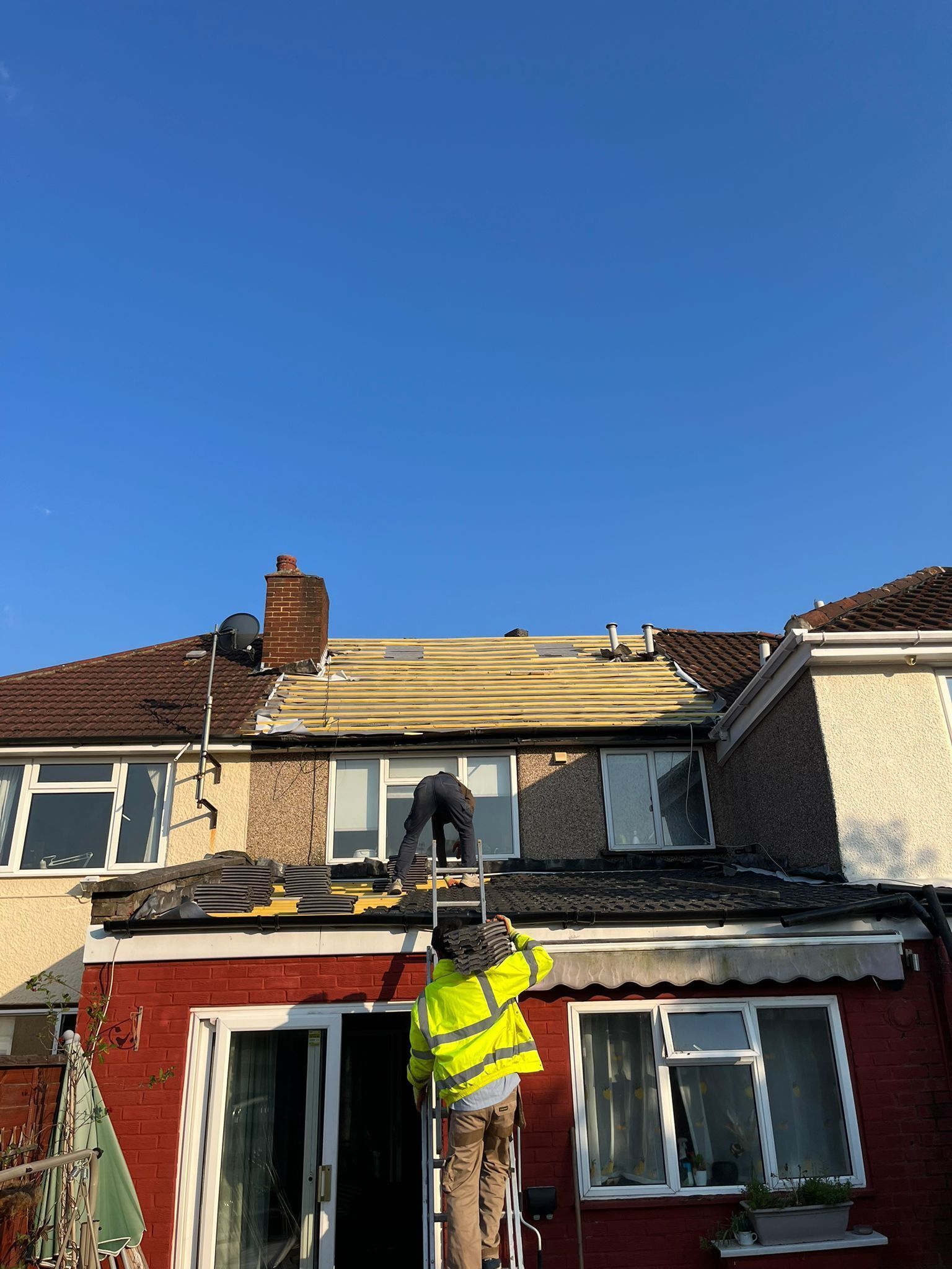 A man is standing on a ladder working on the roof of a house.