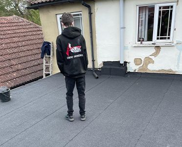 A man in a black hoodie is standing on a roof next to a house.