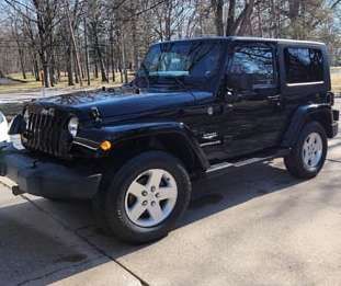 A black jeep wrangler is parked in a driveway.