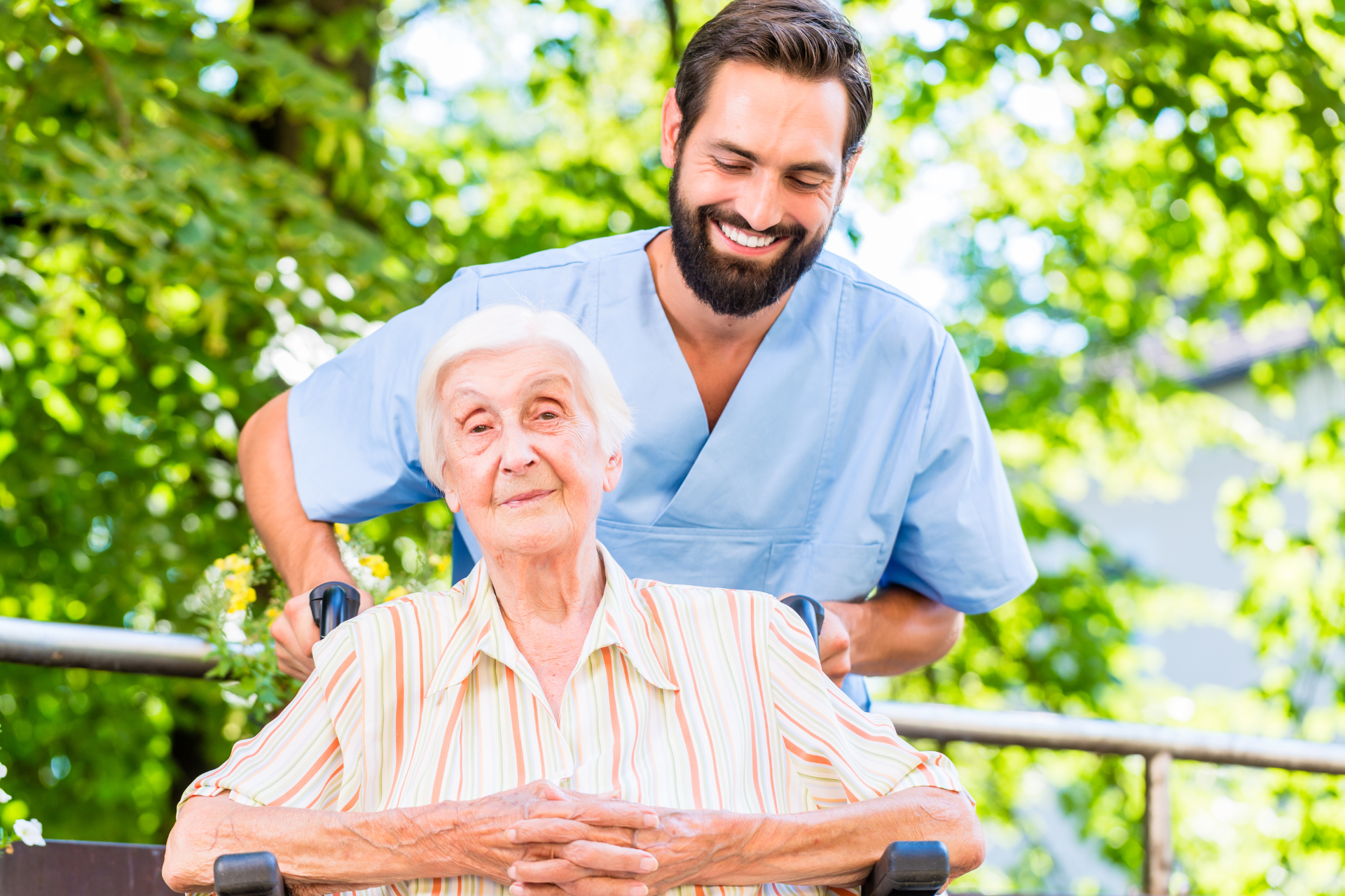 a male healthcare practitioner pushing an older woman in a wheelchair as they both laugh