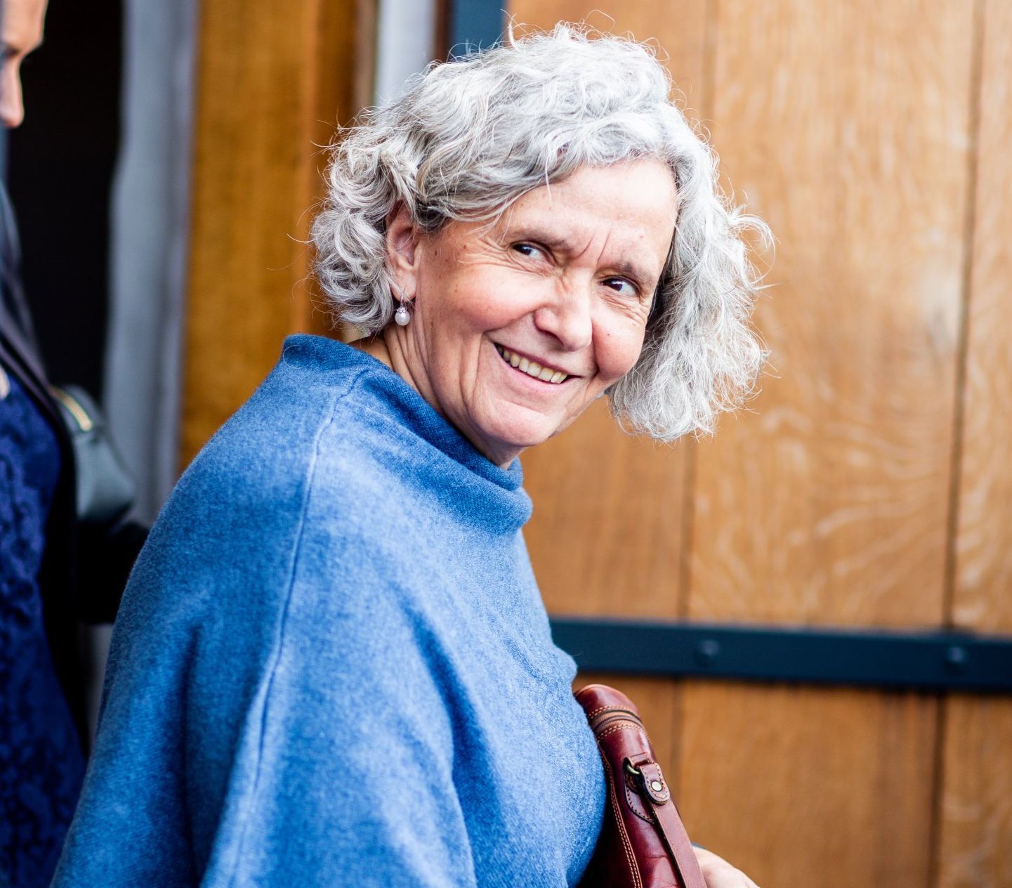 A woman with gray hair is wearing a blue poncho and smiling.