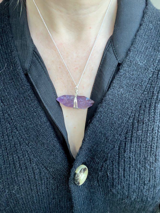 A woman wearing a black sweater and a purple necklace.