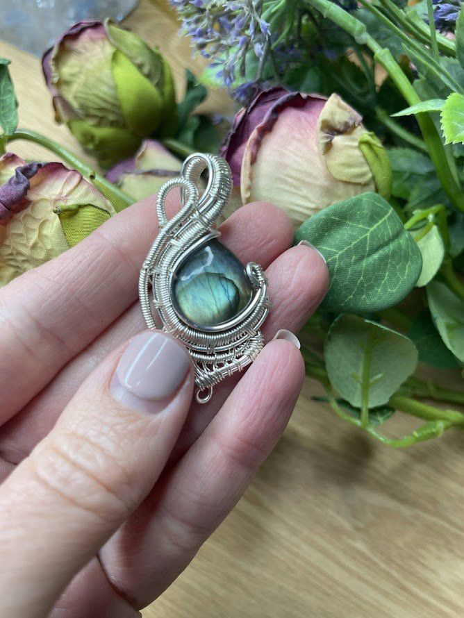 A person is holding a pendant in their hand in front of a bouquet of flowers.