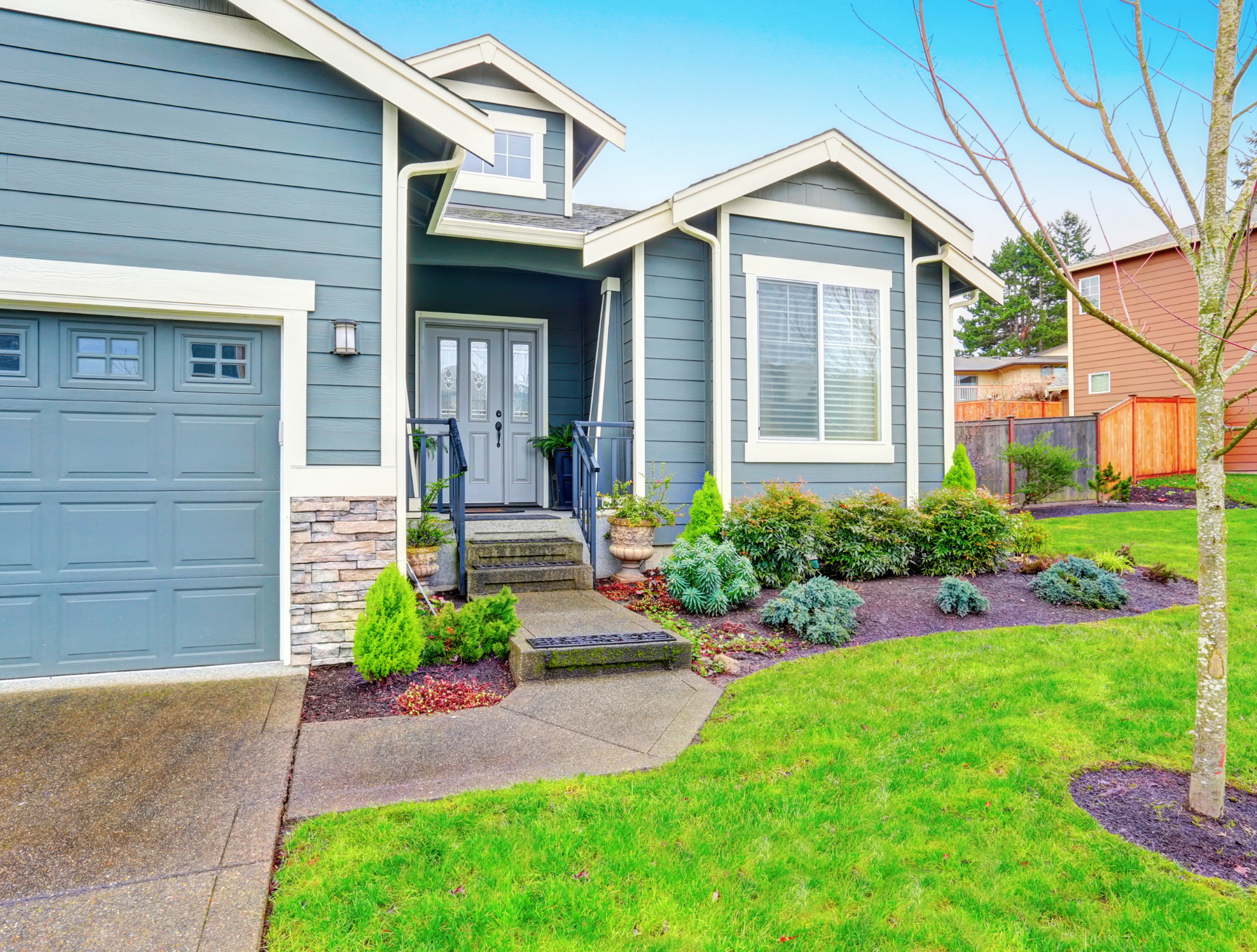 A blue house with a large garage door and a lush green lawn.
