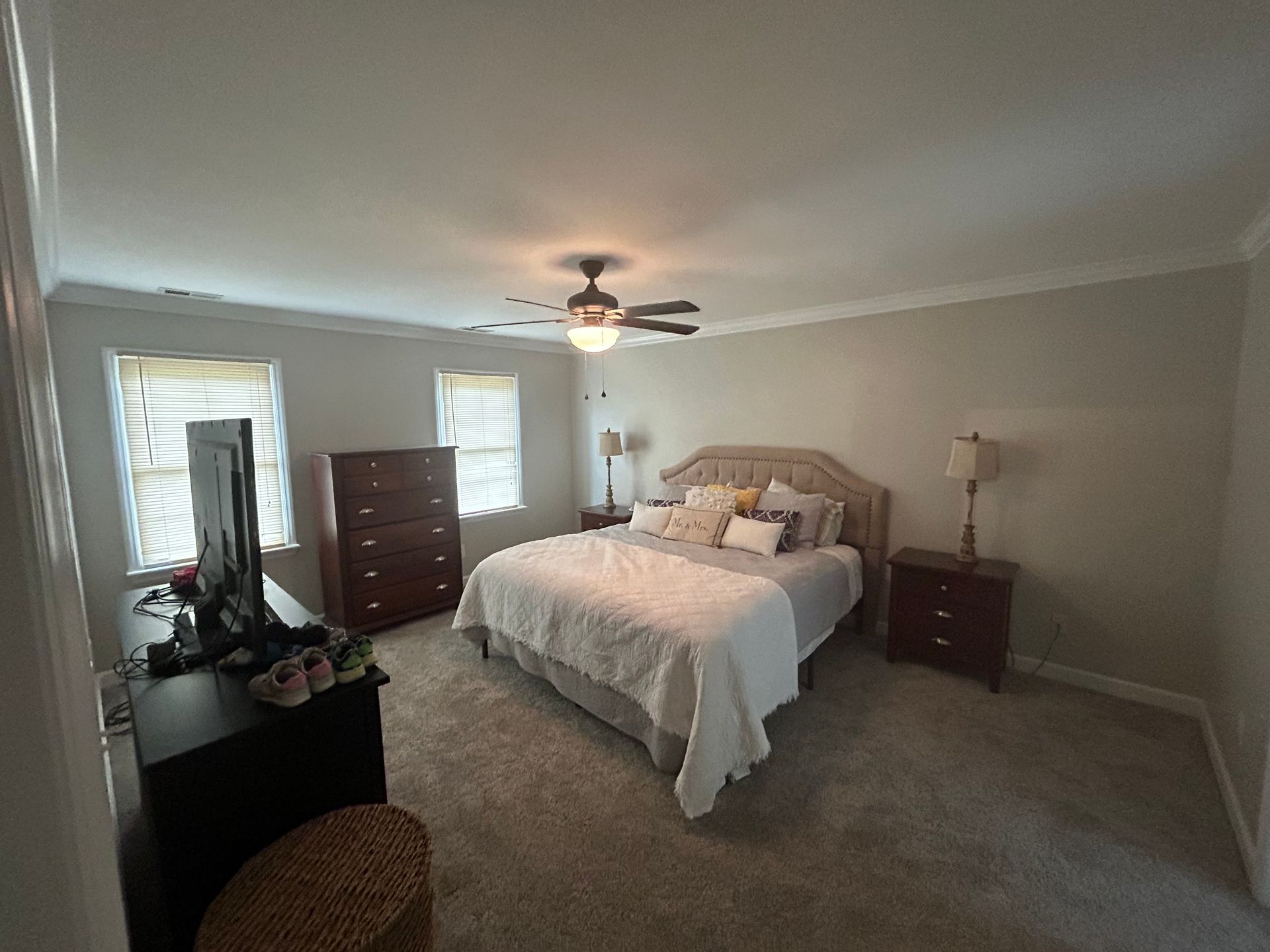 A bedroom with a bed , dresser , nightstand , television and ceiling fan.