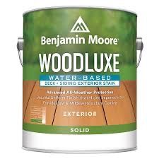 A can of Benjamin Moore Woodluxe solid, water-based exterior stain for decks and siding, featuring a wood-toned background.