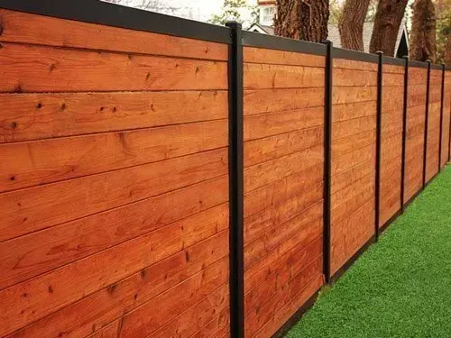 A horizontal cedar wood fence with black metal posts and trim panels, set against green grass and trees.