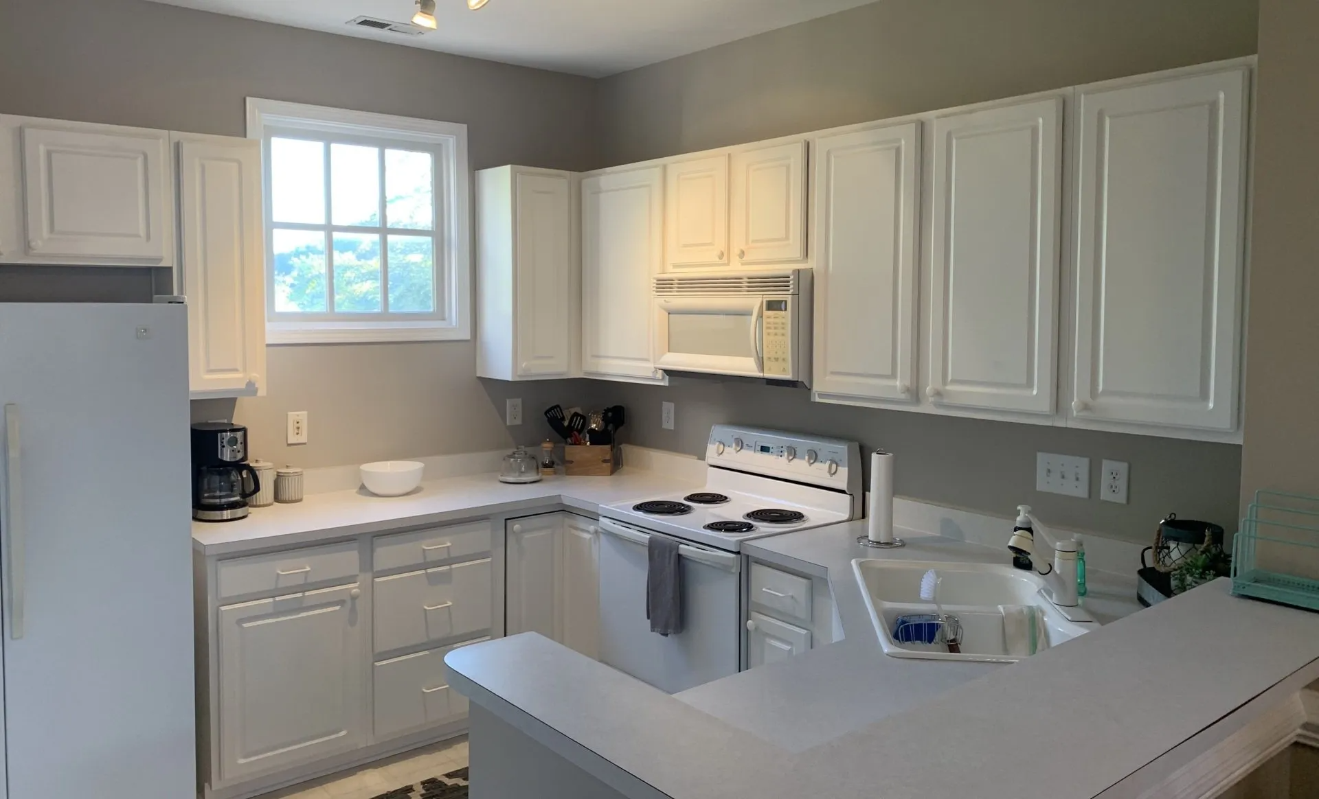 A kitchen with white cabinets , white appliances , and a window.