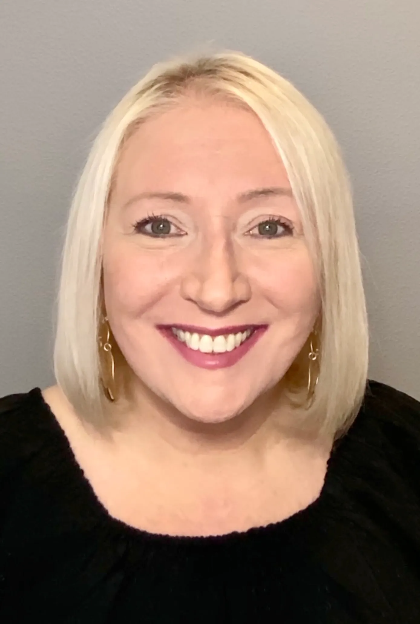 A woman with blonde hair and earrings is smiling for the camera.