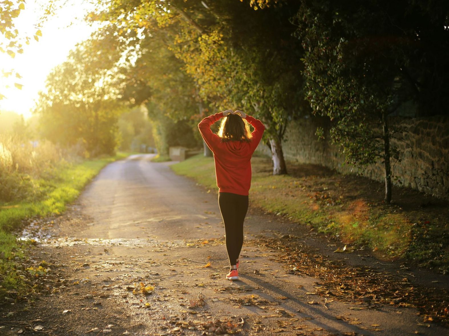 A woman is walking down a road with her hands on her head.
