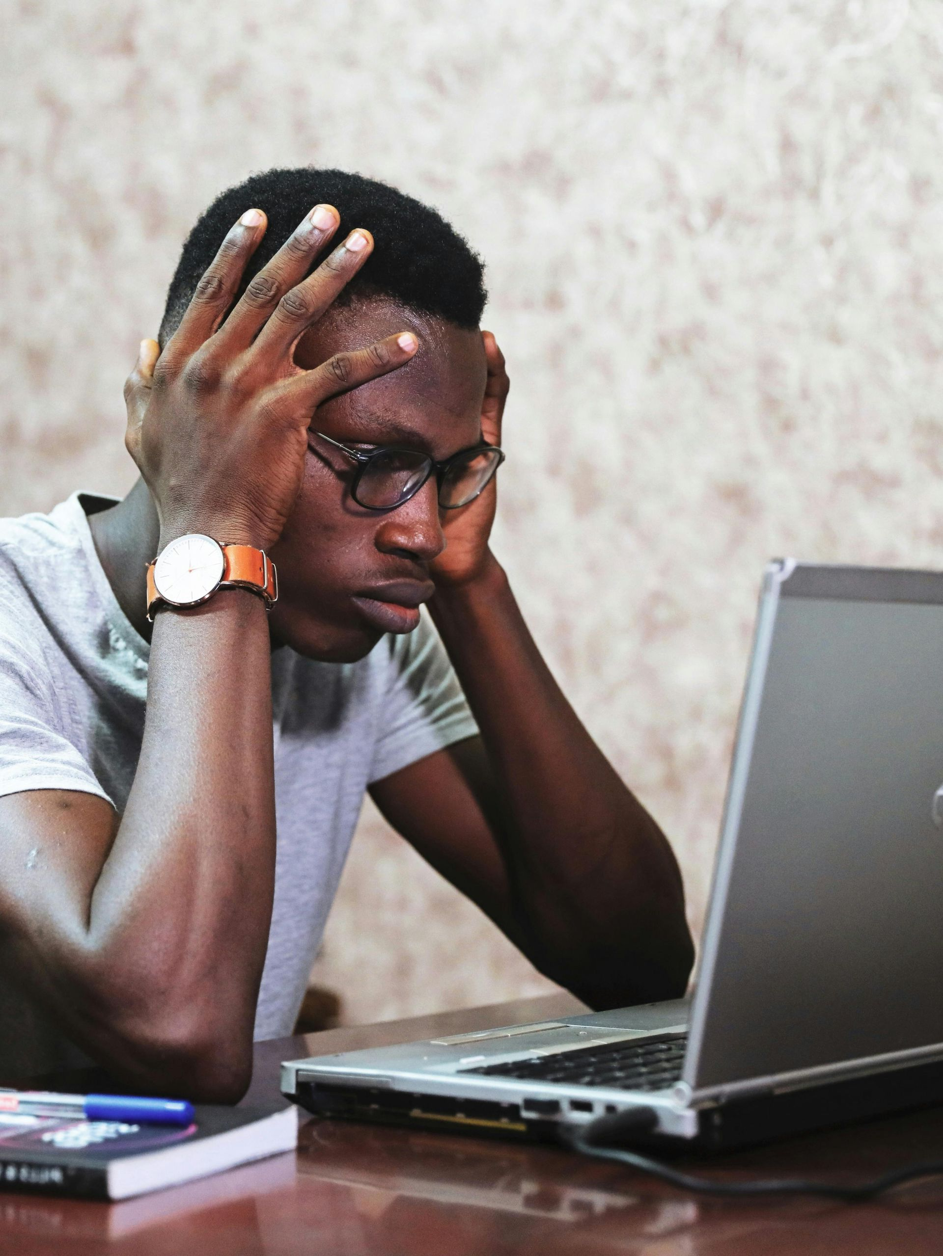 A man is sitting at a desk with his hands on his head in front of a laptop computer.