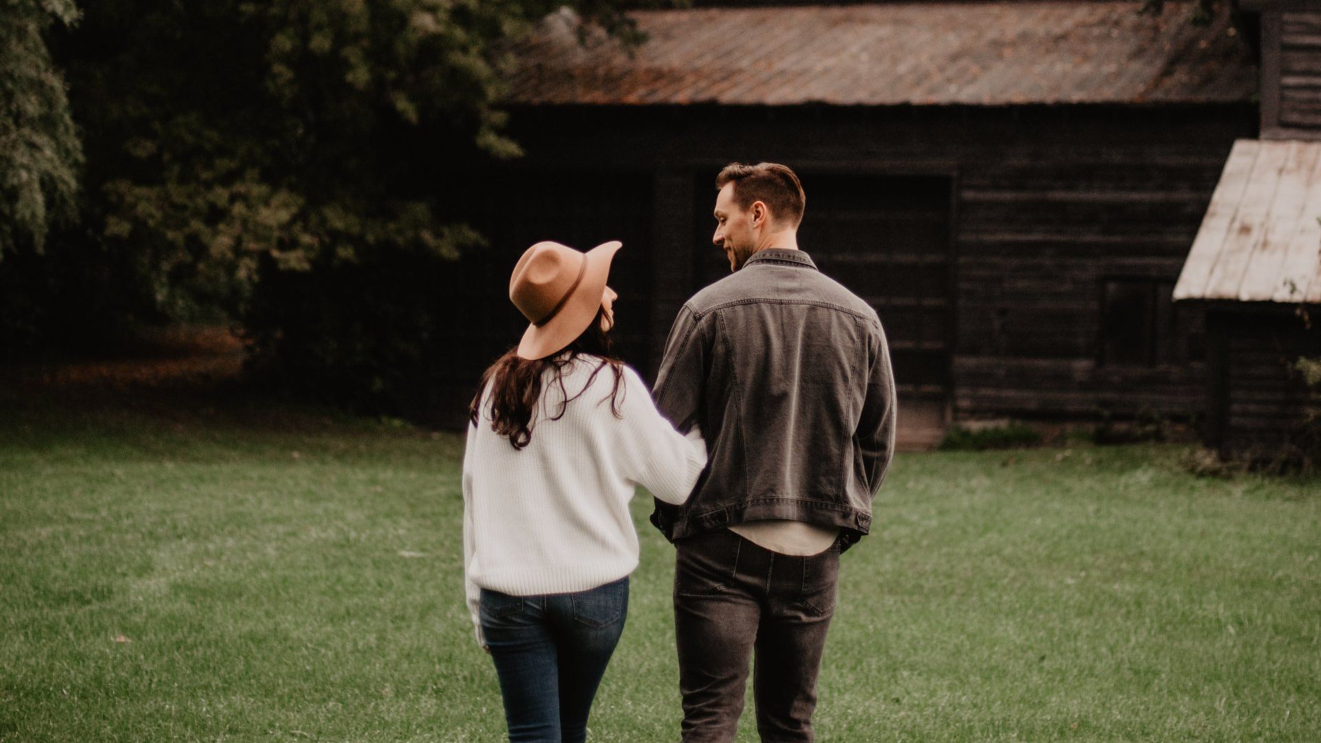 A man and a woman are walking in a field in front of a barn.