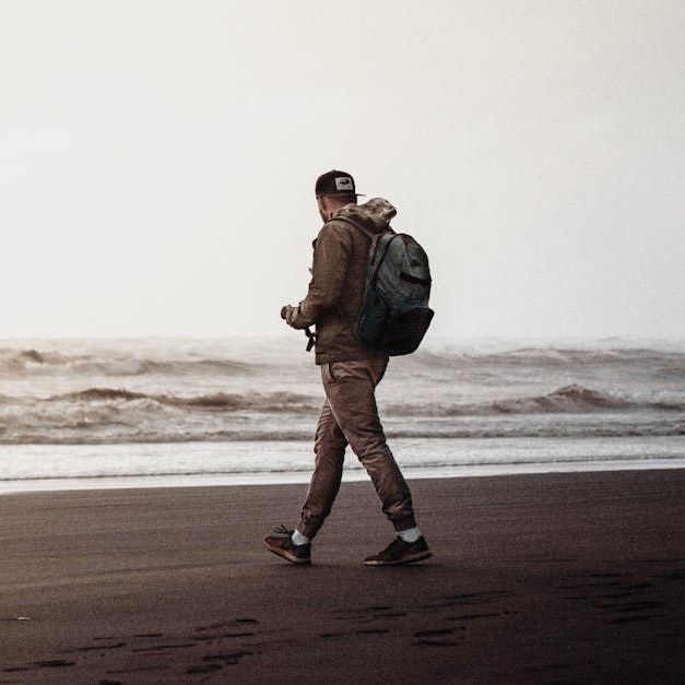 A man with a backpack is walking on the beach