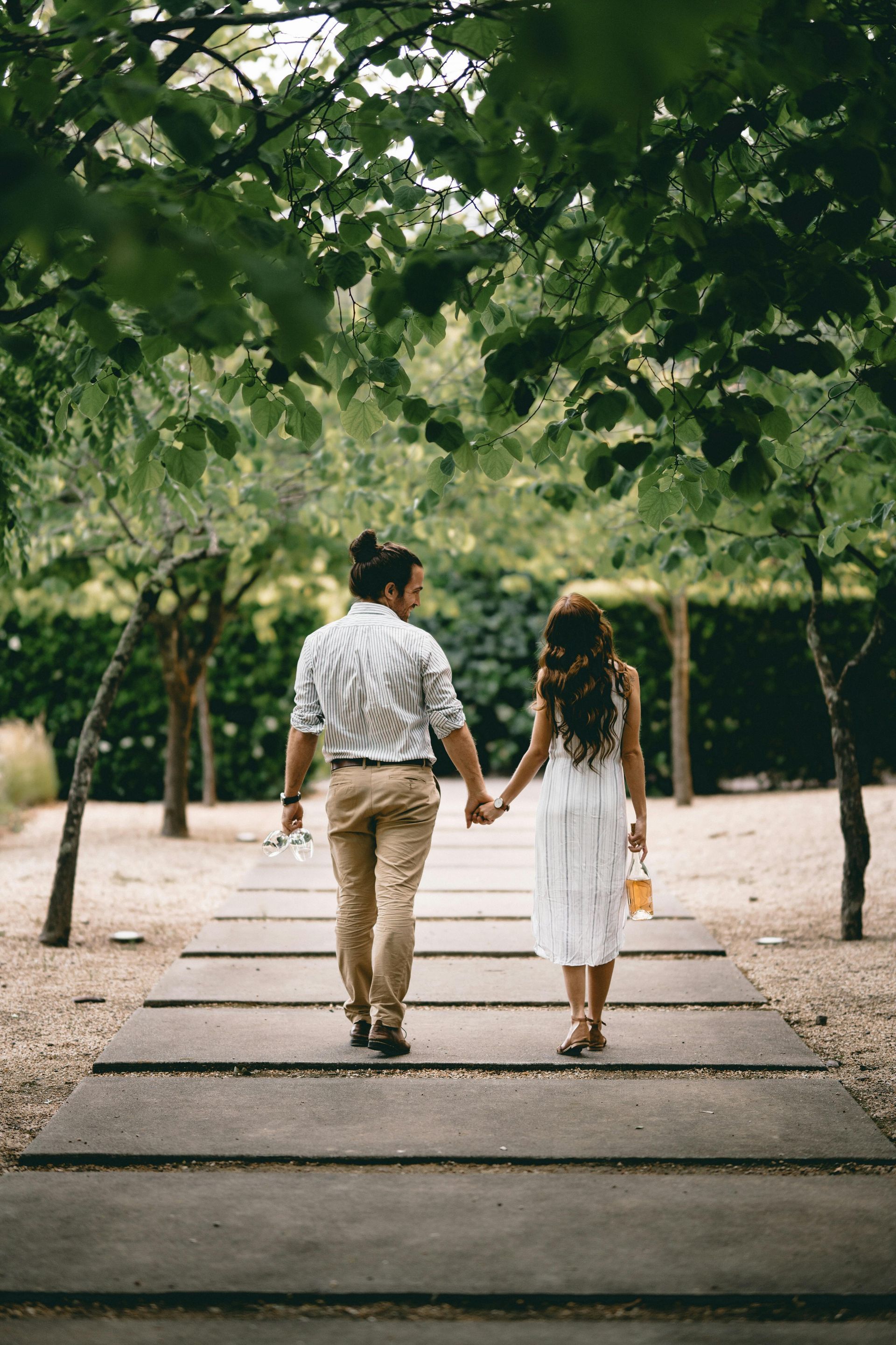 A man and a woman are walking down a path holding hands.