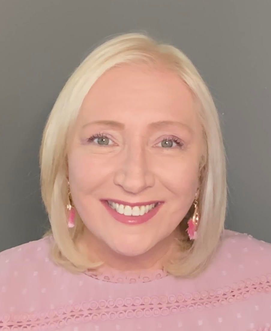 A woman with blonde hair and earrings is smiling for the camera.