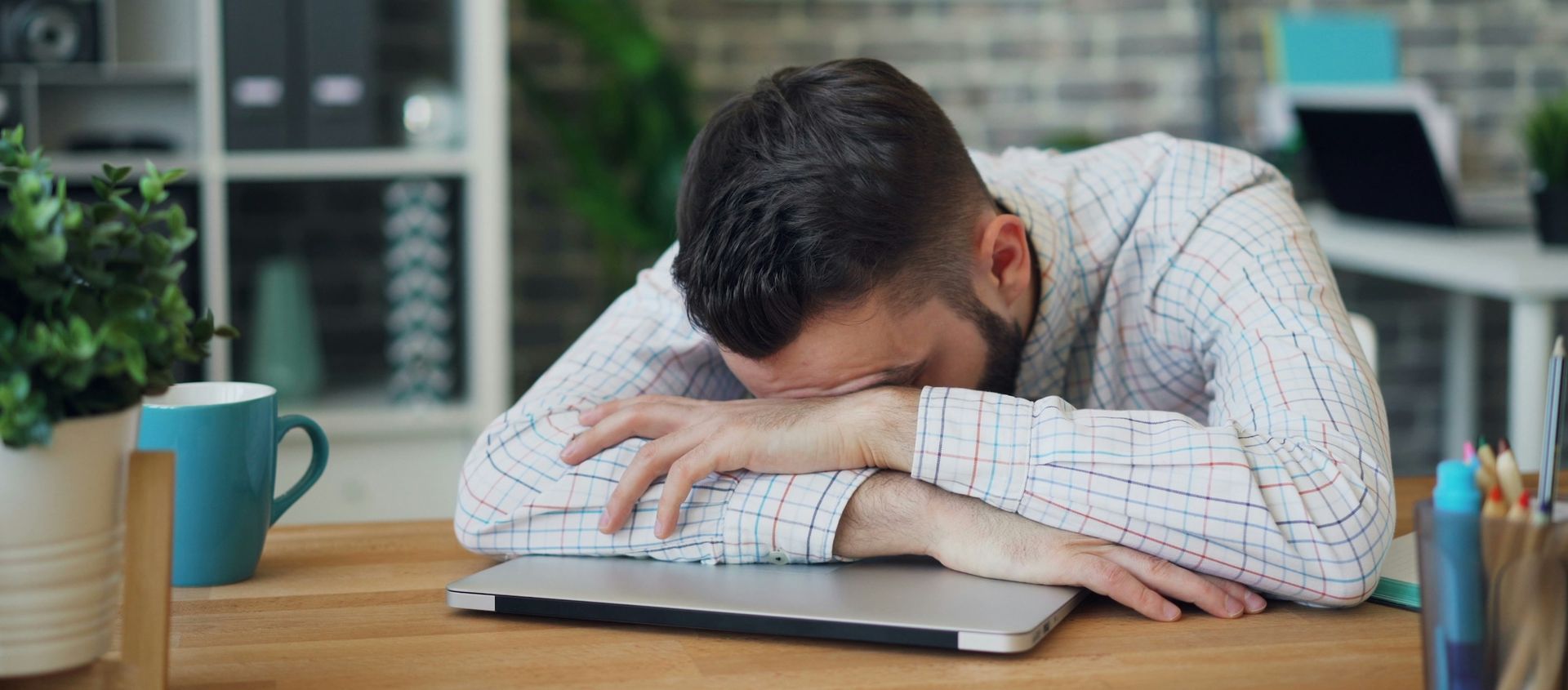 A man is sitting at a table with his head on top of computer.