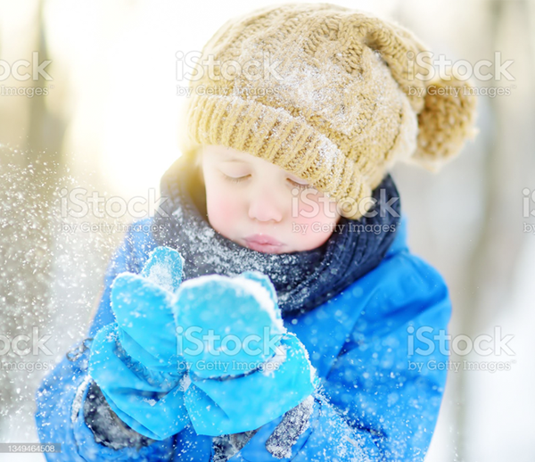 A little boy is blowing snow from his hands in the snow.