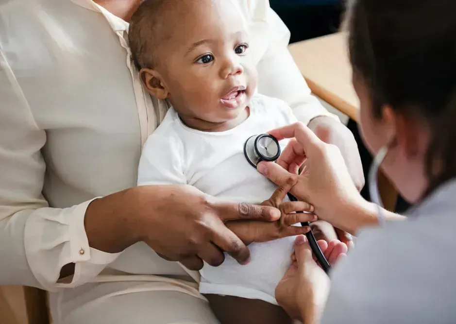 Baby getting heart checked by stethoscope during medical exam.