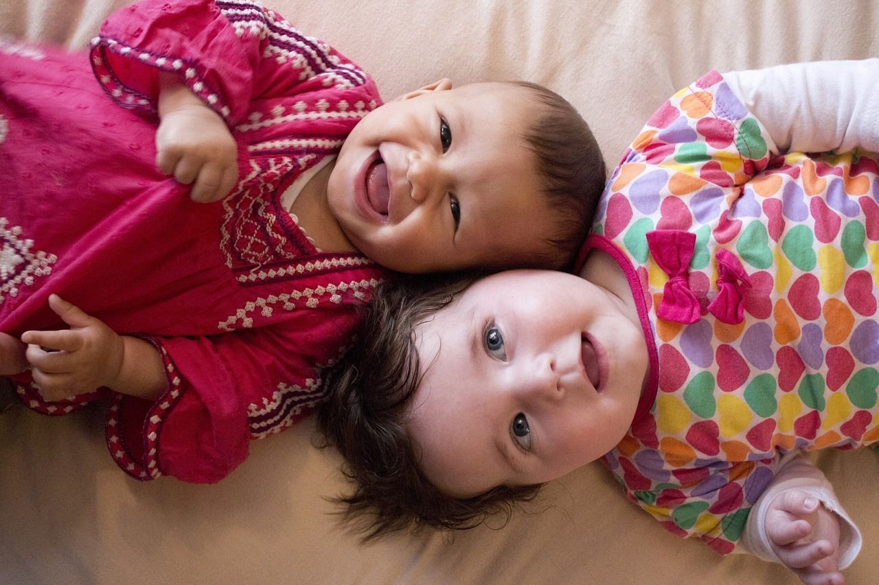 Two babies are laying next to each other on a bed.