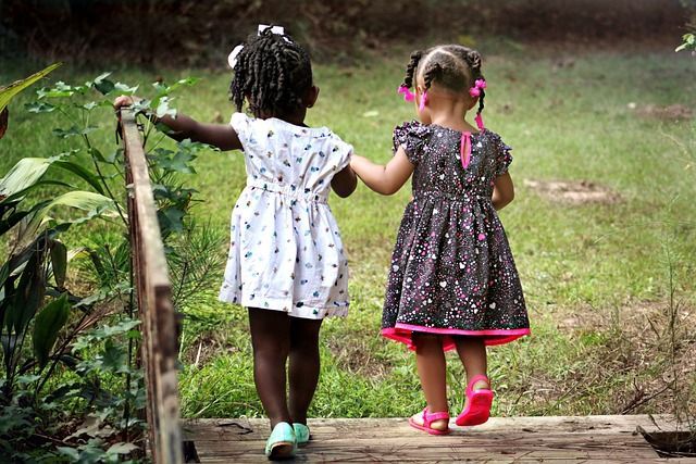 Two little girls are walking across a wooden bridge holding hands.