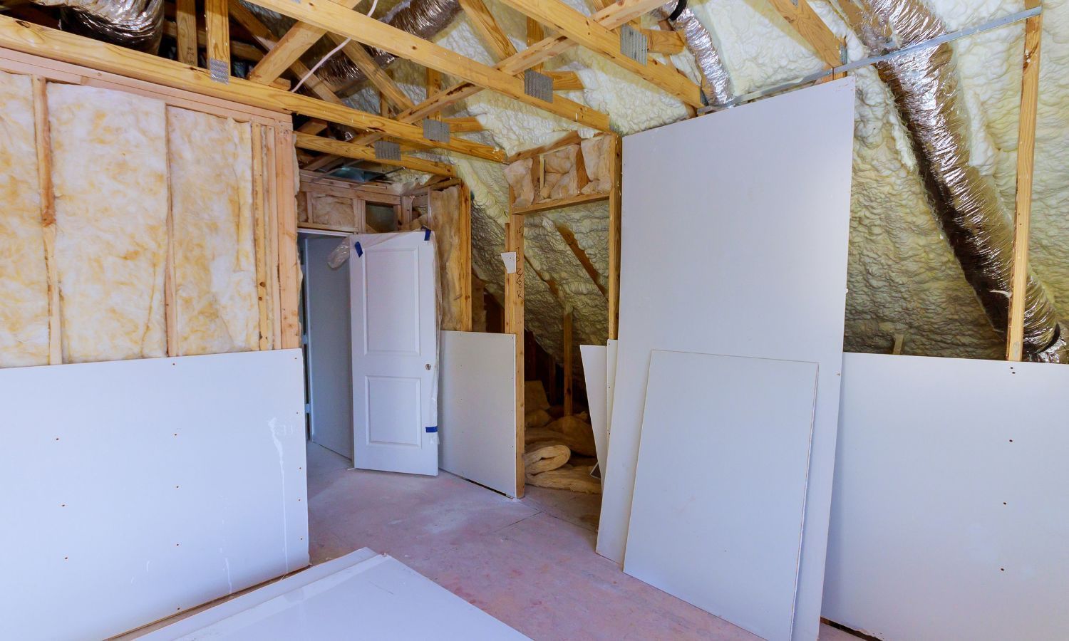 Interior view of an attic under construction with exposed wood, insulation, and drywall.