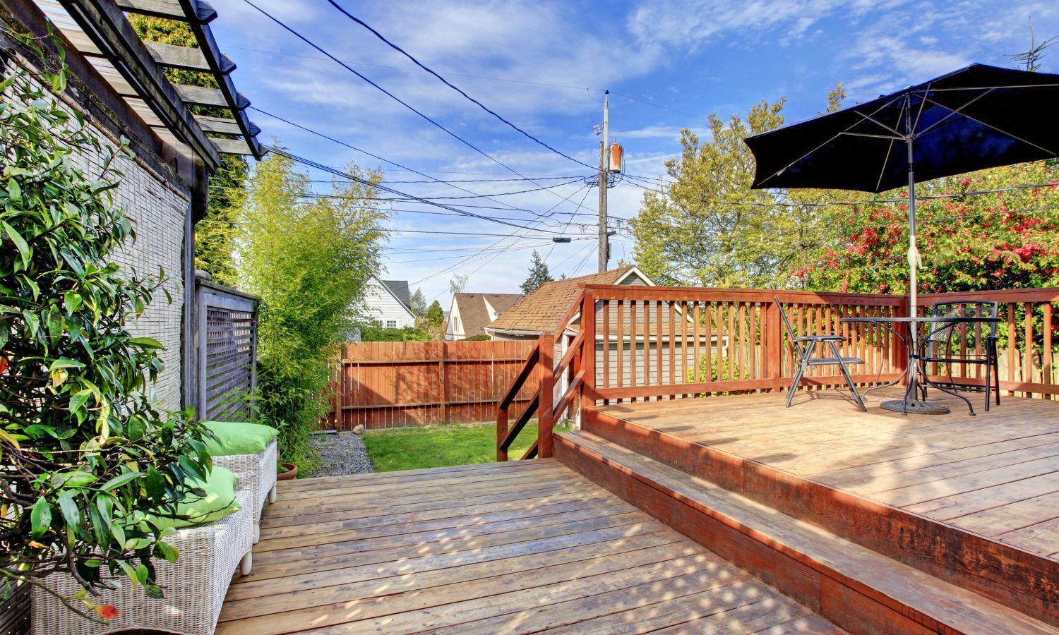Wooden deck with umbrella, table, and seating next to a fenced yard, with sky in the background.