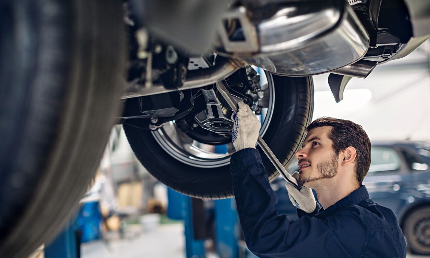 Mechanic working on the underside of a car in a garage, using a wrench.
