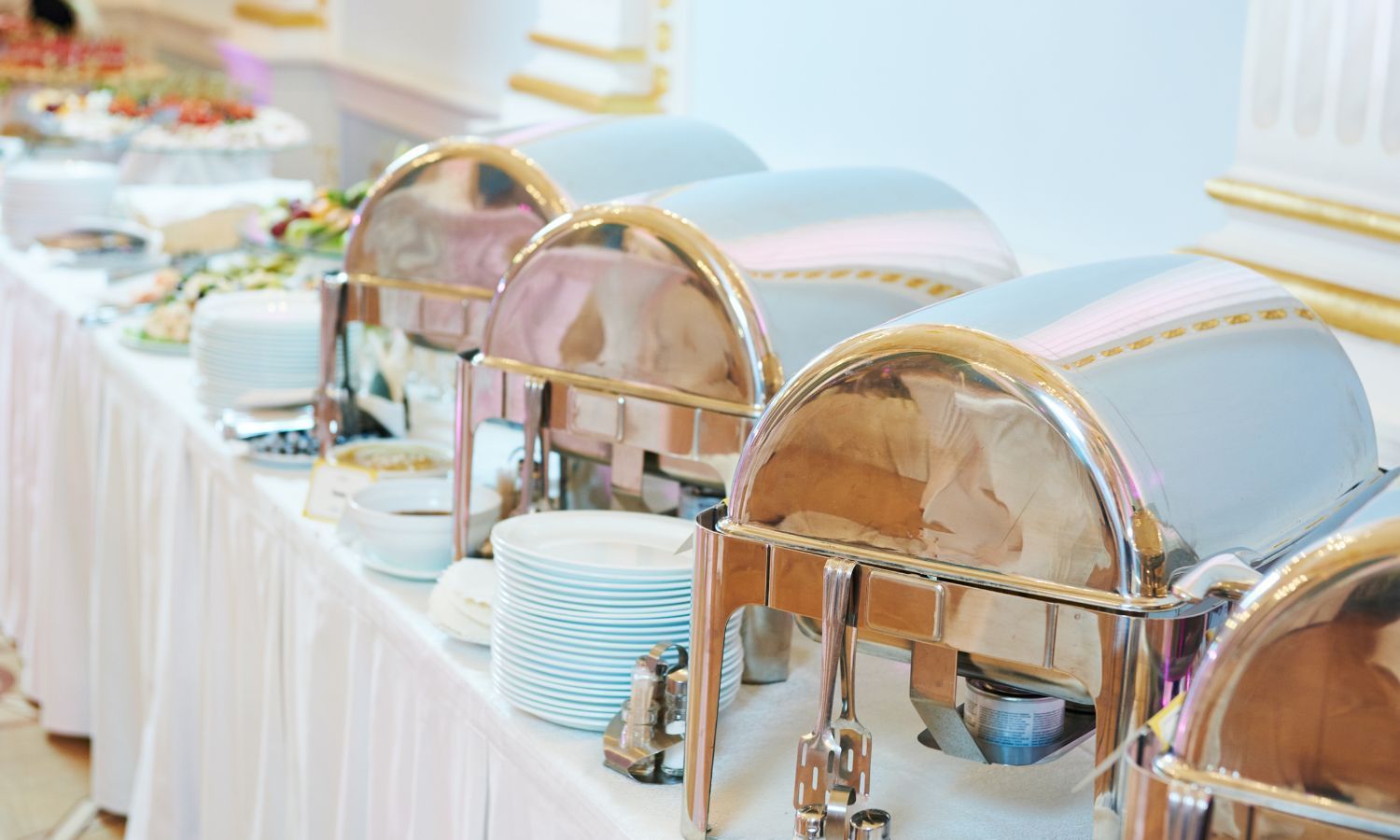Buffet table with silver chafing dishes and white serving ware.