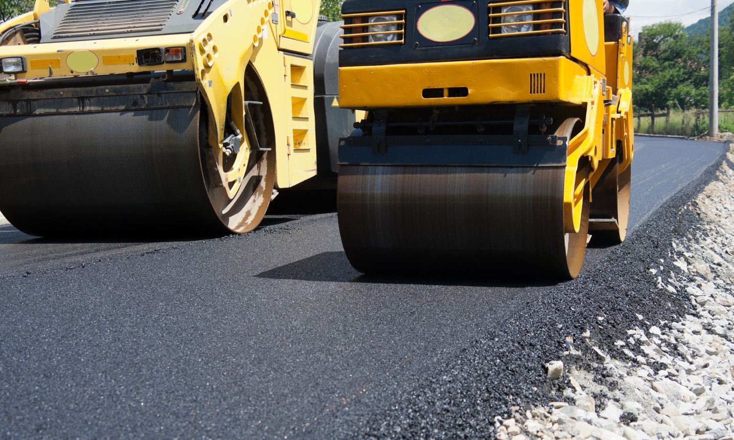 Two yellow road rollers compacting fresh asphalt on a new road.